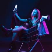 Mulher dentro de uma carrinho de compras segurando celular para comprar via redes sociais