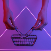 Tendência de consumo 2024: duas mãos seguram pelas alças uma cesta de mercado num fundo rosa neon